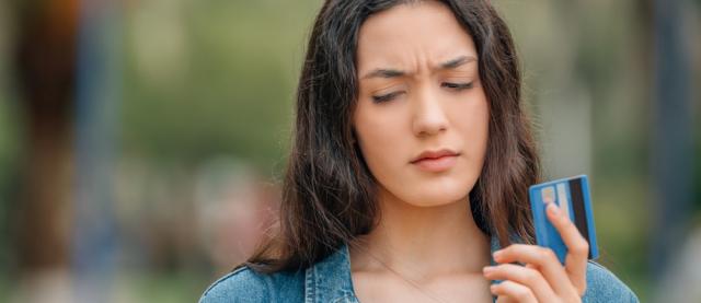 Vrouw met bankpas in hand kijkt verontrust naar telefoon