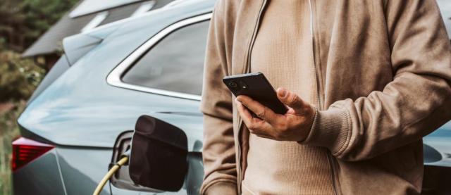 Man wacht met mobiel in de hand terwijl auto laad