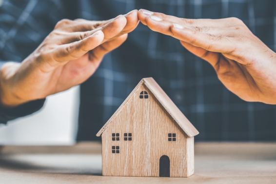 Twee handen vormen samen een dakje boven een miniatuurhuis