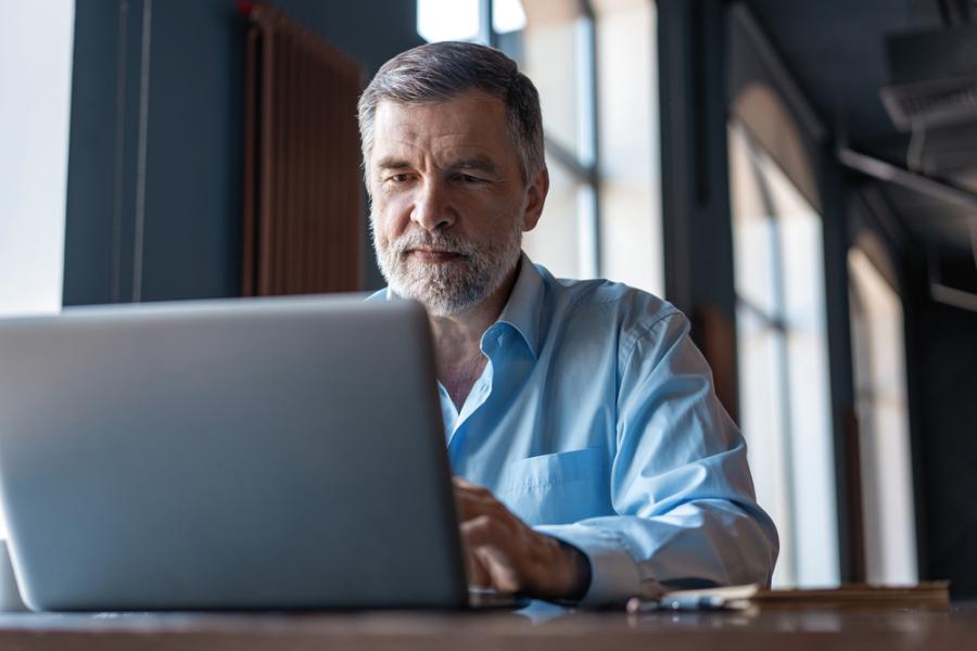 Man 67+ werkend achter laptop