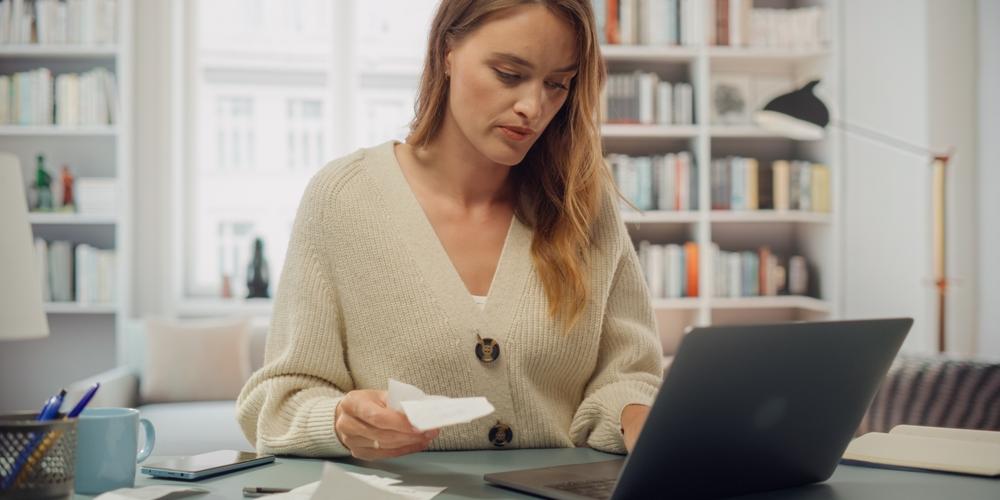 Vrouw achter laptop met kassabon in handen